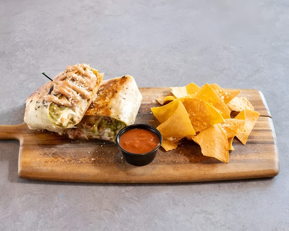 Grilled burrito with sauce and cheese, served with tortilla chips and salsa on a wooden board.