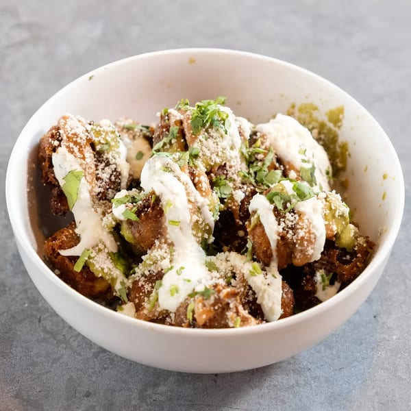 A white bowl filled with crispy fried brussels sprouts, drizzled with white sauce, green sauce, and cilantro.