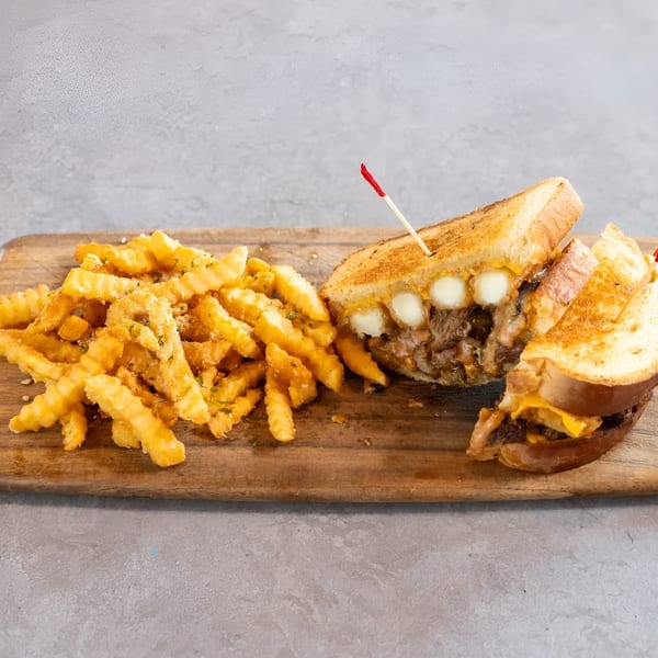 Grilled cheese sandwich with meat and cheese curds, served with crinkle-cut fries on a wooden board.